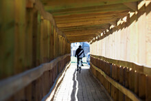 Looking Down The Inside Of A Covered Wooden Bridge. Lonely Cyclist On A Wooden Corridor-bridge