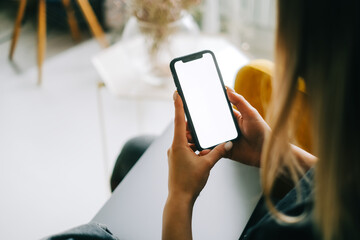 woman holding mobile phone with white screen mock up, resting on a sofa in living room at home.