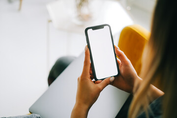 woman holding mobile phone with white screen mock up, resting on a sofa in living room at home.