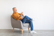 Leinwandbild Motiv Portrait of mature man using smartphone sitting on armchair