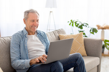 Wall Mural - Confident casual mature using pc sitting on sofa