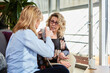 © SteelStock - Friends drinking coffee on sofa. Two mature women in glasses sitting on sofa with mug of coffee.