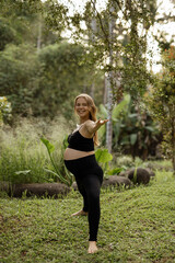 Wall Mural - Healthy happy pregnant woman in black clothes doing yoga in the park in nature outdoors