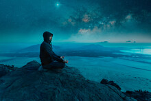 Person Sitting On The Top Of The Mountain Meditating At Night With Stars And  Milky Way Background