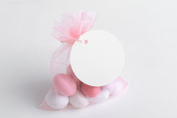 Wall Mural - Round white tag mockup with gift with pink chocolate confetti in a bag with pink ribbon. Wedding favor tag for souvenir o gift for gues, sign for message greeting, close up, element for design