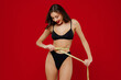 © ViDi Studio - Young slender thin slim satisfied fun woman 20s with perfect fit body wearing black underwear hold measure tape on waist isolated on plain red background studio portrait. People female beauty concept