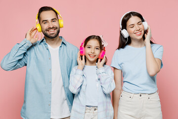 Wall Mural - Young happy smiling cheerful parents mom dad with child kid daughter teen girl in blue clothes headphones listen to music have fun isolated on plain pastel light pink background. Family day concept.