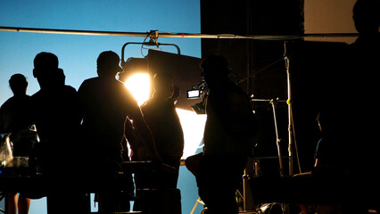 Behind the scenes of video production shooting studio in silhouette which have professional equipment such as camera, tripod and blue screen backdrop set for chroma key technique in post process and m