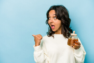 Wall Mural - Young hispanic woman holding a honey isolated on blue background points with thumb finger away, laughing and carefree.