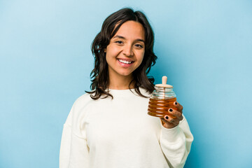 Wall Mural - Young hispanic woman holding a honey isolated on blue background happy, smiling and cheerful.