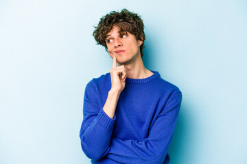 Wall Mural - Young caucasian man isolated on blue background contemplating, planning a strategy, thinking about the way of a business.