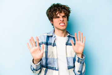 Wall Mural - Young caucasian man isolated on blue background rejecting someone showing a gesture of disgust.