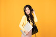 Portrait of happy casual Asian girl student with backpack, headphones and laptop isolated on yellow background. Back to school and learning concept.