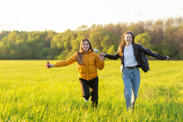 Wall Mural - Mom and daughter casual dressed run in field at beautiful spring sunset.