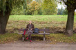 Cute young short haired blonde woman sitting on the bench and relaxing in the autumn park.