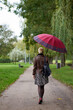 Young stylish short haired blonde woman walks in the autumn park with red umbrella. View from back.