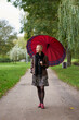 Attractive smilling short haired blonde woman walking in the autumn park with huge red umbrella.