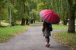 Stylish young woman walks in the autumn park with huge red umbrella. View from back.