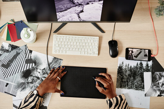 Top view of female photo retoucher using pen tablet while editing pictures at workplace, copy space