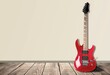 Electric guitar with wooden body and fret board stands the background of a brick wall.