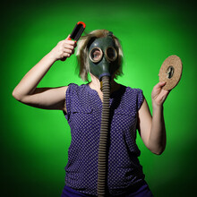 Blonde Woman In A Gas Mask Combs Her Hair And Looks At The Camera On A Dark Background