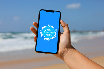 Wall Mural - Woman holding phone with card for World Ocean Day on screen outdoors