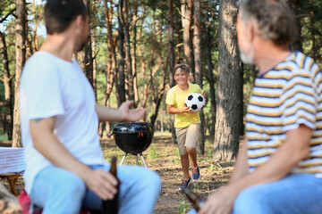 Little boy with ball running to his father and grandfather in forest