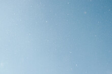 Falling Snow, White Snowflakes On Clear Blue Sky Outdoors. Defocus Light Slow Snowfall In Winter