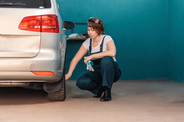 Wall Mural - A female mechanic inspects a car tire in an auto repair shop. The concept of women's work in male professions