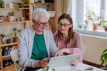 Wall Mural - Adult daughter visiting her senior father at home and using tablet.