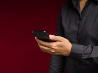 Wall Mural - businesswoman in a black shirt hand holding a smartphone while standing on a red background