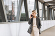 © anatoliycherkas - Portrait of a beautiful mature business woman in suit and gray jacket smiling and talking on the phone on a modern urban and office buildings background