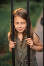 The Girl Is Standing Behind A Fence With Bars And Trying To Climb..
