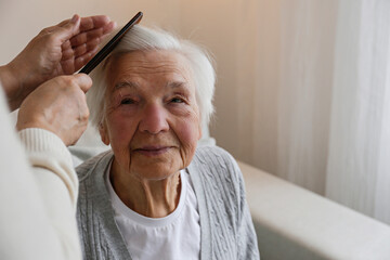 unrecognizable female expressing care towards an elderly lady, brushing her hair with a comb. grandd