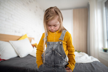 Sad little girl with Down syndrome looking down at home.