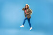 Full length of young African American female traveller running with backpack, jumping up in air over blue background