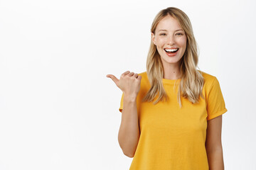 Sticker - Portrait of happy smiling cute girl, woman pointing finger left at copy space, logo banner, company advertisement, standing against white background