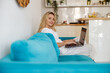 © Kostiantyn - Portrait of blonde beautiful female smiling to camera while working on laptop at home.