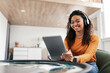 © Prostock-studio - Smiling black woman in headset using tablet in living room