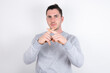 © Roquillo - Young handsome dark haired man wearing fitted T-shirt over white wall Has rejection angry expression crossing fingers doing negative sign.