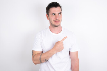 Young handsome dark haired man wearing fitted T-shirt over white wall Pointing aside worried and nervous with forefinger, concern and surprise concept.