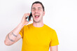 © Roquillo - Overemotive happy Young caucasian man wearing yellow t-shirt over white background laughs out positively hears funny story from friend during telephone conversation