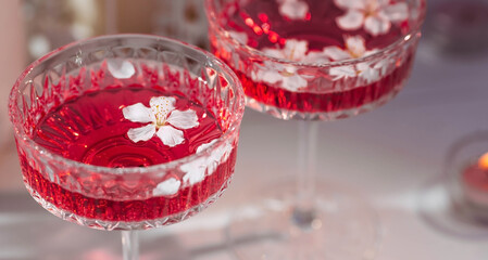 Two fashionable glasses for dessert and champagne with a pink drink and cherry blossoms inside on a light background with hard shadows and highlights. The concept of a party and a holiday.