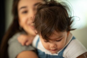 Wall Mural - Cute little baby toddler pouncing and jumping while in the arms of young mother hugging at home