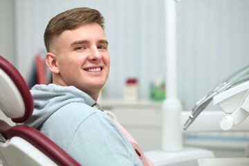 Portrait of happy satisfied smiling with white teeth young man patient with perfect smile, positive guy having a seat, sitting on dentist medical chair in dental office after treatment in clinic 