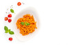 Flatlay composition of fusilli pasta with paprika pesto sauce and basil leafs in porcelain plate and cherry tomatoes, and pepper grains around on white isolated background