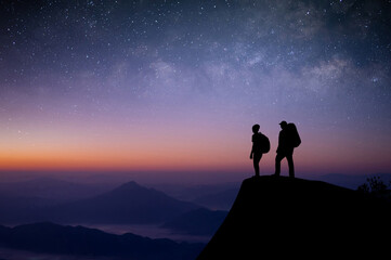Wall Mural - Silhouette of two young traveler with backpack standing on top of the mountain watched the beautiful view of night sky, star and milky way. We are happy to travel with friend in the wide world.