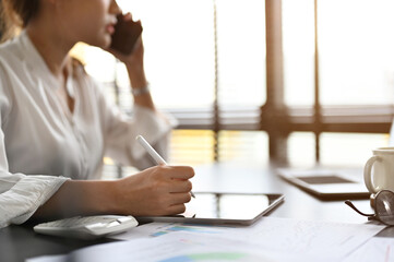 asian businesswoman talking on the phone while using digital tablet at her desk.