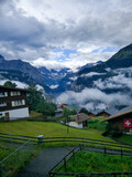 Fototapeta Tęcza - Lauterbrunnen, Switzerland - August 19, 2019: Beautiful view of the Alpine Lauterbrunnen valley with wooden chalets in the Jungfrau region. White clouds cover the mountains. Vertical