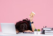 Young tired business woman in casual shirt sit work and sleep laid her head down on white office desk with pc laptop, she is holding cup coffee isolated on pastel pink background.